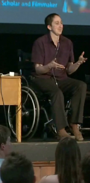 Picture of Danielle on a stage, in her wheelchair, giving a talk