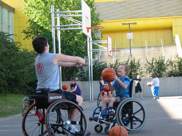 Picture of Danielle using her arms as a basketball hoop for a young wheelchair basketball athlete